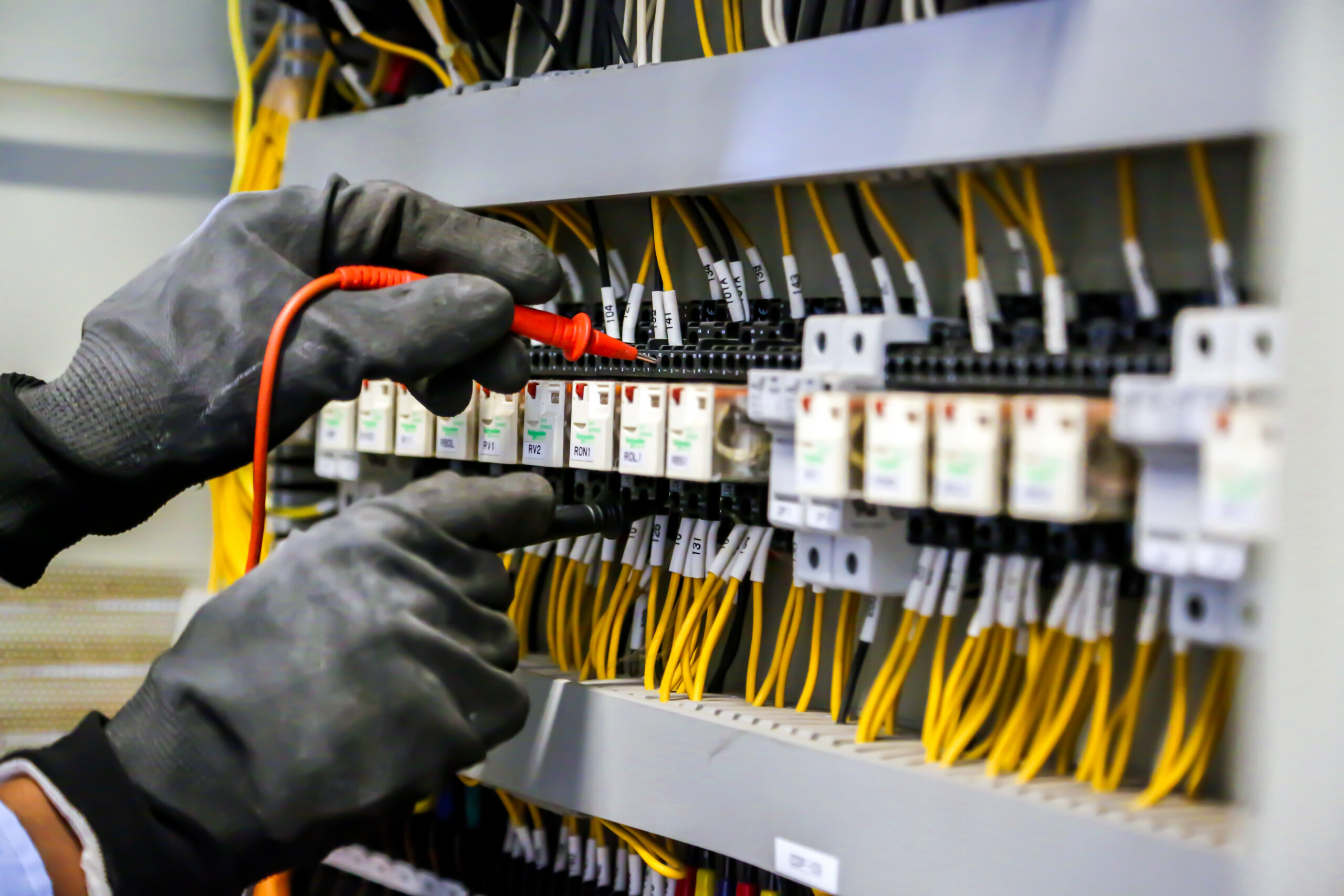 Electrical engineer using digital multi-meter measuring equipment to checking electric current voltage at circuit breaker in main power distribution board.
