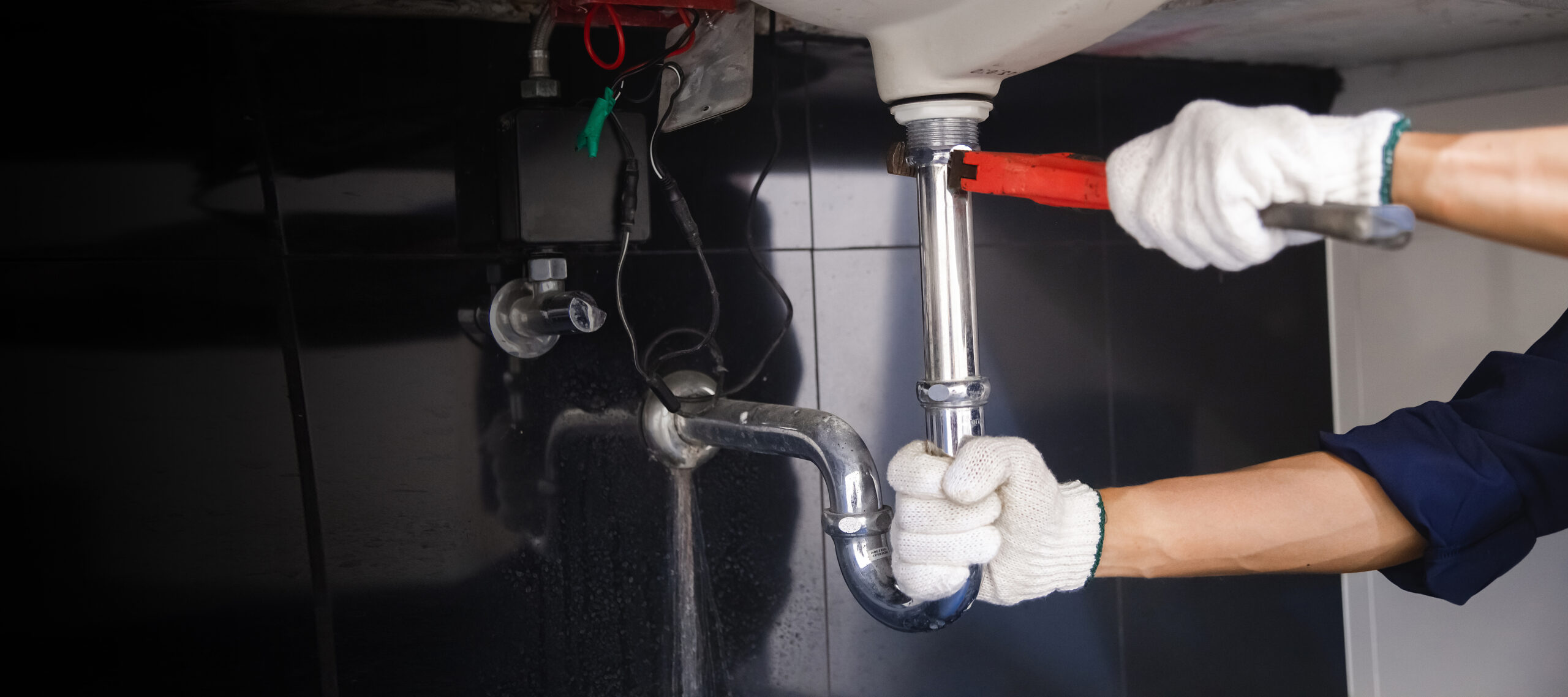 Plumber fixing white sink pipe with adjustable wrench.