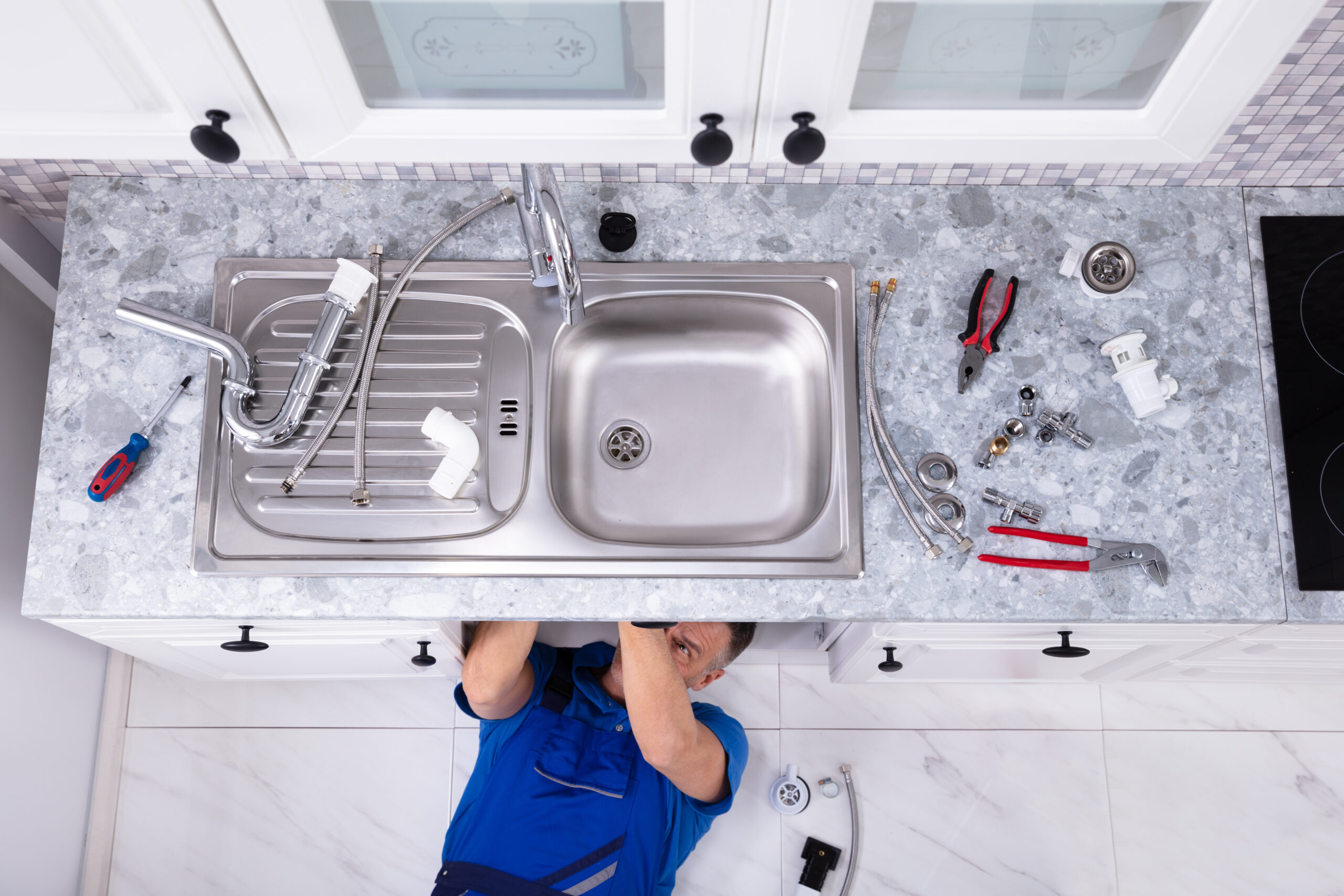 Plumber lying on the floor fixing pipes under a kitchen sink