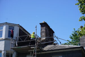 A roofer carrying various tools to a roof via scaffold placed in front of a house in Aberdeen